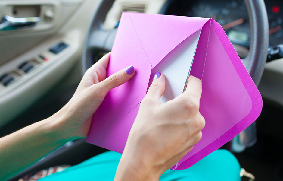 A woman putting an invitation into a pink envelope.